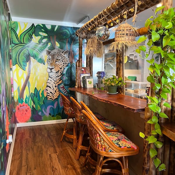Tropical-themed bar with a jaguar mural, bamboo accents, and rattan stools with floral cushions.