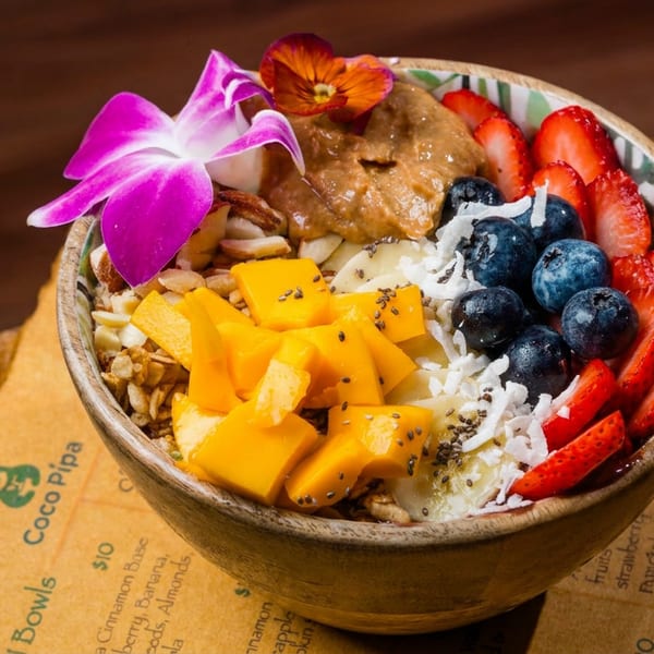 A vibrant Coco Pipa acai bowl with mango, blueberries, strawberries, peanut butter, and a purple orchid.