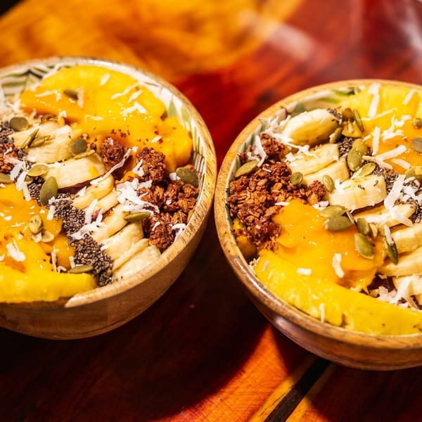 Two vibrant smoothie bowls topped with mango, banana, granola, seeds, and coconut flakes.