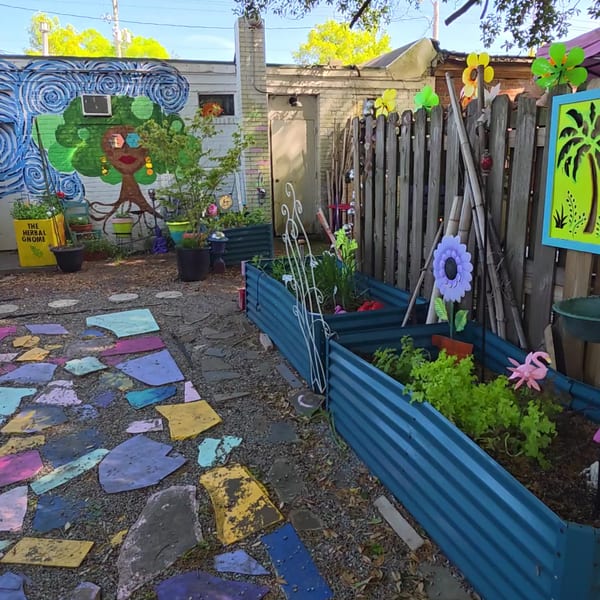 A vibrant backyard garden with colorful stepping stones, raised beds, and a whimsical mural on a brick wall.