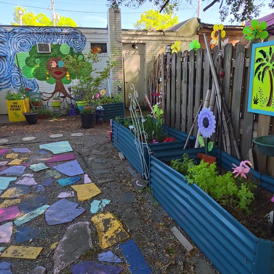 A vibrant garden with colorful stepping stones, raised beds, and a whimsical mural on a brick wall.