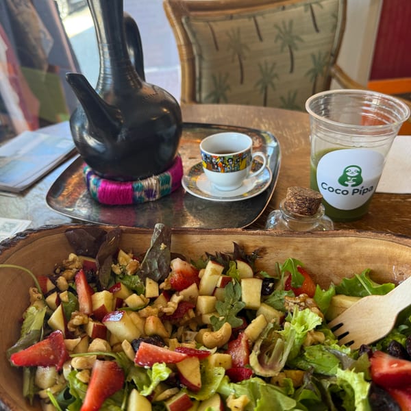 A fresh salad with strawberries, apples, and nuts, alongside a green juice and coffee.